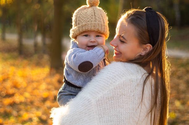 Happy family on autumn walk. Mother holds little son in her arms and enjoying the beautiful autumn nature in a park. Mother's day concept